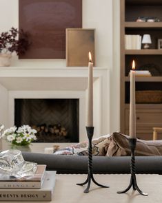 two candles sitting on top of a table in front of a fire place and books