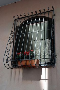 a window with iron bars and flower pots on the sill, in front of a pink wall