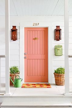 an orange front door on a white house with potted plants and watering cans next to it