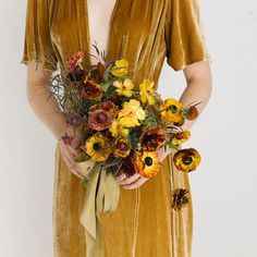 a woman in a velvet dress holding a bouquet of sunflowers and greenery