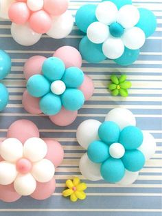 there are many small flowers made out of fondant on the counter top, and one is pink, white, blue, and green