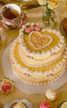 a heart shaped cake sitting on top of a table next to cupcakes and flowers