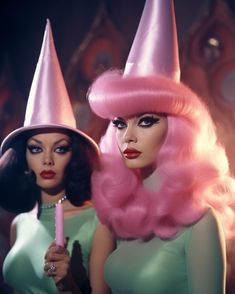 two women dressed in pink wigs and hats, one holding a candle while the other holds