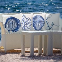 three pillows sitting on top of white wicker chairs next to the ocean with blue and white seashells