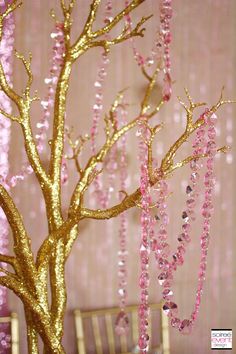 a gold tree with pink beads hanging from it's branches in front of a wall