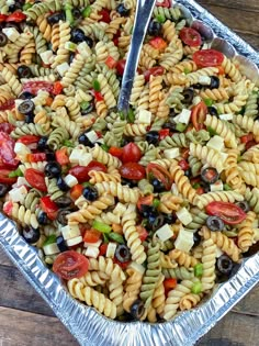 a pasta salad with olives, tomatoes and green peppers in a silver serving dish