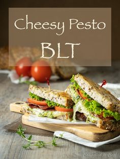 a cut in half sandwich sitting on top of a cutting board next to tomatoes and bread