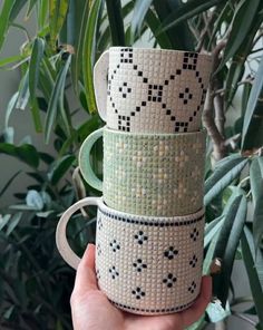 three coffee mugs are stacked on top of each other in front of a potted plant