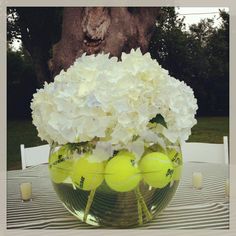 a vase filled with tennis balls sitting on top of a table next to a tree