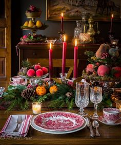 a dining room table set for christmas dinner with candles and fruit on the table top