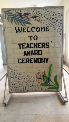 a welcome sign for teachers'award ceremony in front of a brick wall with leaves and flowers painted on it