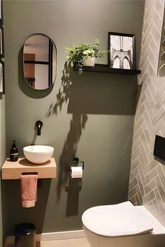 a bathroom with a toilet, sink and mirror next to a plant on the wall