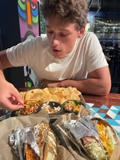 a man sitting at a table with some tacos and chips in front of him