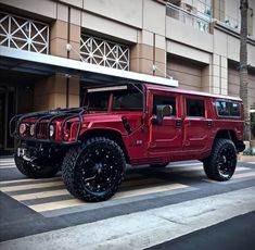 a red hummer truck parked in front of a building with black wheels and tires