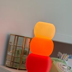 an orange and red lamp sitting on top of a white shelf next to a phone