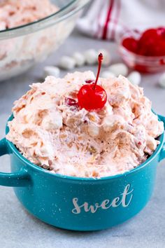 a blue bowl filled with whipped cream and a cherries on the top, next to another bowl full of candy