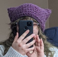 a woman wearing glasses and a knitted hat holds her cell phone up to her face