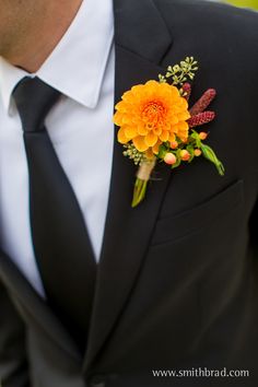 a man wearing a black suit and orange flower boutonniere