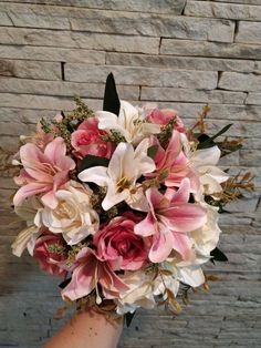 a woman holding a bouquet of pink and white flowers in front of a brick wall