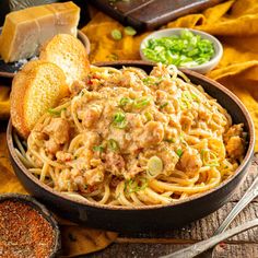 a bowl filled with pasta and meat on top of a wooden table next to bread