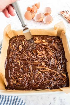 someone is spreading chocolate frosting on top of an uncooked cake in a pan