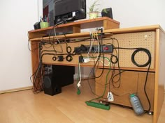 a computer desk with many cords and remotes on top of it in front of a television