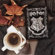 a harry potter book next to a cup of coffee on a table with autumn leaves