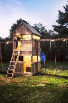 a child's wooden play house with swings and lights on the roof is lit up at night