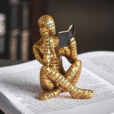 a gold statue sitting on top of an open book holding a cell phone in it's hands