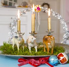 three small figurines sitting on top of a plate with grass and candles in the middle