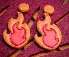 two orange and pink earrings on top of purple carpet with circles in the middle that are shaped like hearts