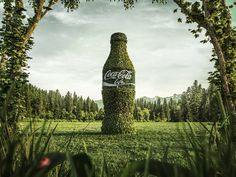 a giant bottle covered in grass sitting on top of a lush green field next to trees