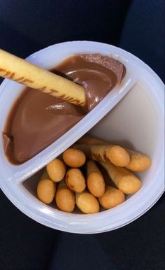 a plastic bowl filled with peanut butter and chocolate covered pretzels next to a stick