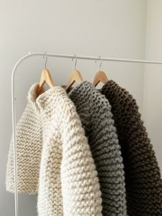 three sweaters hanging on a clothes rack in a white room with wooden hangers