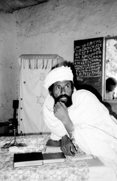 an old photo of a man sitting at a table in front of a blackboard