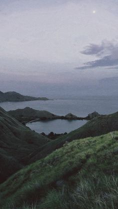 an image of some hills and water at night time with the moon in the sky