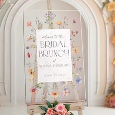 a sign with flowers on it in front of a floral arch for a bridal brunch