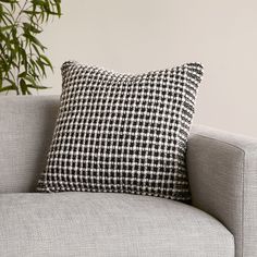 a black and white checkered pillow sitting on top of a gray couch next to a potted plant