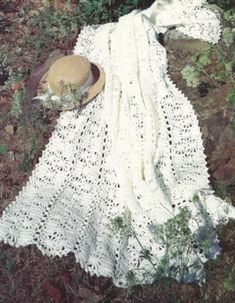 there is a white crocheted blanket and hat on the ground next to plants