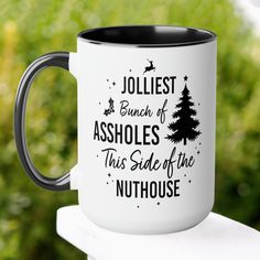 a white and black coffee mug with the words jolliest bunch ofahbles this side of the nuthouse on it