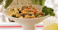 a white bowl filled with pasta salad on top of a table next to a green plant