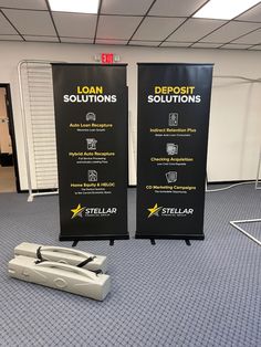 two roll up banners on the floor in an empty room with one laying on the ground