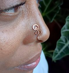 a close up of a person with a nose ring on their nose and leaves in the background