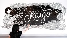 a woman is drawing on the wall with black and white lettering that says kaugo