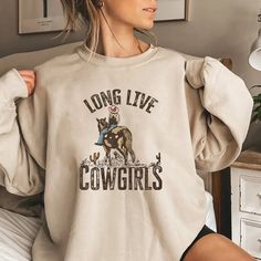 "\"Long Live Cowgirls\" Sweatshirt: Celebrating the Spirit of the Wild West Saddle up and embrace the untamed spirit of the Wild West with our \"Long Live Cowgirls\" sweatshirt. Crafted for those who embody strength, independence, and a love for adventure, this sweatshirt is a tribute to the fearless spirit of cowgirls everywhere. 🤠🐎 Features: Premium Quality: Made from soft, cozy fabric, our sweatshirt ensures warmth and comfort during chilly days on the ranch or casual outings in town. Stylish Design: With its bold and vibrant print featuring the words \"Long Live Cowgirls,\" this sweatshirt makes a statement wherever you go. The classic font and Western-inspired graphics capture the essence of cowboy culture with a modern twist. Versatile Wear: Whether you're wrangling cattle, hitting Outfit Country, Sweatshirt Western, Country Outfit, Music Sweatshirts, Fearless Women, Zach Bryan, Music Tees, Cowboys Shirt, Cow Girl