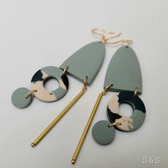 two pieces of green and gold are hanging from the ear hooks on a white surface