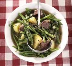 a white bowl filled with meat and green beans on top of a checkered table cloth