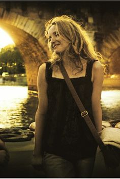 a woman standing in front of a bridge with her eyes closed and looking off to the side