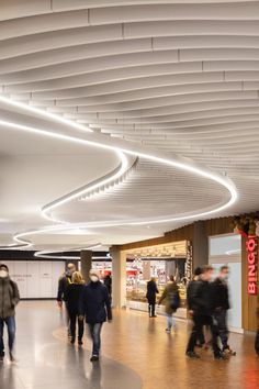 many people are walking around in a large room with circular lights on the ceiling and overhead lighting