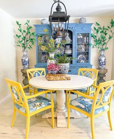 a dining room table with yellow chairs and blue china cabinet in the back ground area